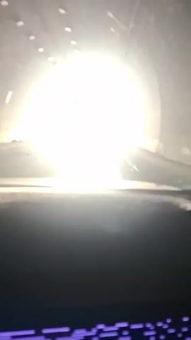 The video shows the interior of a car as it drives through a tunnel and then emerges into a mountainous landscape. The car is moving forward, and the view is from the driver's perspective. Initially, the tunnel is bright, and the car moves towards the light at the end. Once outside, a road stretches ahead with a backdrop of snow-capped mountains under a partly cloudy sky. The road appears clear, and the overall environment suggests a high-altitude location.