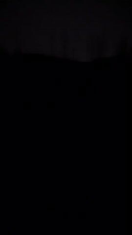 The video shows the moon shining brightly through dark, hazy clouds. The moon appears as a bright, round disc with a faint ray of light extending downwards. The rest of the sky is a dark gray, obscured by the clouds.