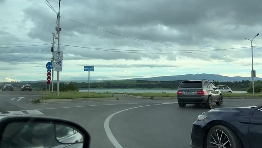 Afternoon traffic flows along lakeside road near Tbilisi mountains