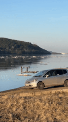 Russian train passes riverbank with parked cars