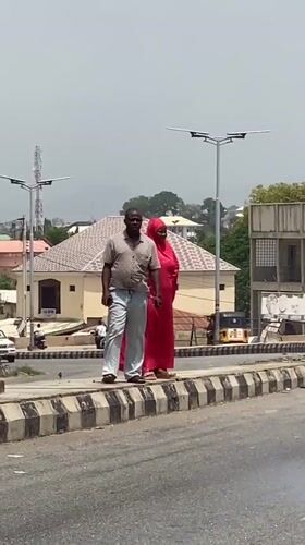 Two pedestrians walk along striped curb in Lokoja, Nigeria