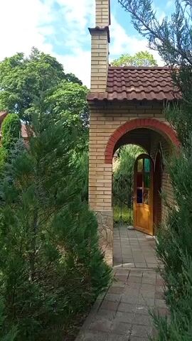A man's voice asks, "Look, you have it too." The video pans from a brick structure with an arched entrance to a wooden building with a red roof and a blue dome, presumably a church, partially obscured by trees.