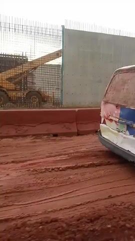 The video pans across a construction site. A yellow construction vehicle is visible behind a metal fence and a concrete wall. In the foreground, a white van with blue and red markings is parked on a dirt road. The van has the text "Hollandia Stay Ahead with Dairy Power" on its side. The environment appears to be dusty and under construction.