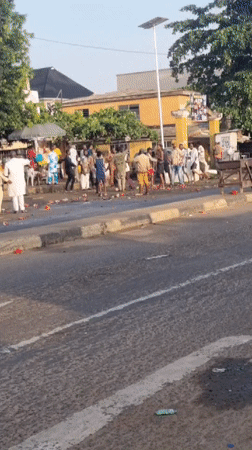 Group gathers on Lagos sidewalk with red objects scattered