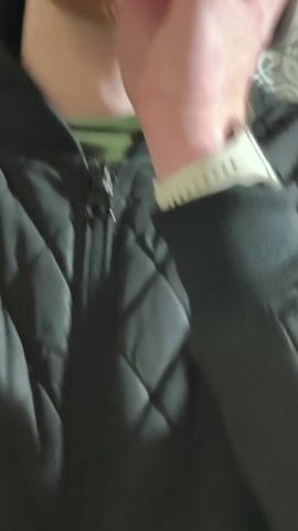 A person is shown indoors, wearing a dark jacket with a ribbed cuff and a light-colored wristband, possibly a smartwatch. Their hands are visible, holding a small metallic object, which appears to be a whistle or a miniature wind instrument. The person is actively blowing into the object, producing a continuous whistling sound throughout the video. In one shot, the camera briefly pans to a window or glass door area. A white lace curtain with intricate patterns is on the left, while a wooden frame and a metal ring with a key hanging from it are visible on the right. Another plaid-patterned curtain is partially visible on the far right. The background behind the person's hands features a white fabric with a repeating grey pattern. No text is visible in the video.