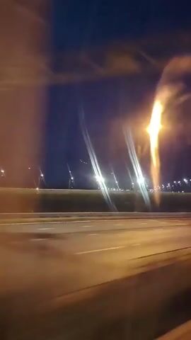 The video shows a nighttime view from a vehicle moving along a highway. Streetlights illuminate the road and the dark sky. A car is visible driving on the highway in the distance, and its headlights are on. The camera is mounted inside another vehicle and captures the passing scenery, including the road, guardrails, and the dark sky. The footage is blurry due to the movement of the camera and the vehicle, creating light streaks from the streetlights.