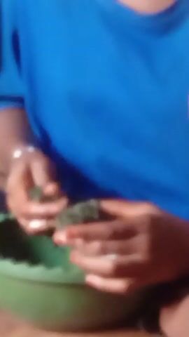 A person wearing a blue t-shirt is sitting in front of a green bowl and manipulating something green in their hands. The object in their hands is out of focus, and the person's hands are slightly wet or oily.
