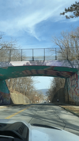 Vehicle travels road beneath mural-decorated pedestrian bridge in Newburgh