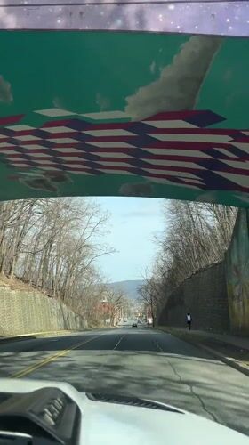 Vehicle travels road beneath mural-decorated pedestrian bridge in Newburgh