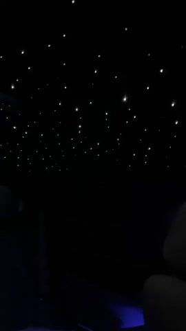The video shows a view from inside a vehicle at night. The ceiling of the vehicle is illuminated with tiny white lights that resemble stars. The lights are scattered across the dark ceiling, creating a starry night effect. Some of the seats are visible in the foreground, appearing dark and indistinct. There is a faint blue light emanating from the lower part of the interior. The video appears to be static with no noticeable movement.