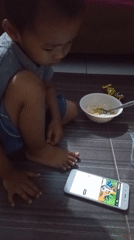 Child sits with smartphone on floor in Lhokseumawe