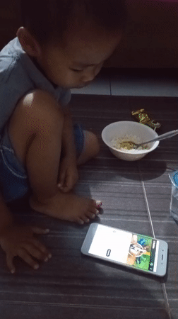Child sits with smartphone on floor in Lhokseumawe