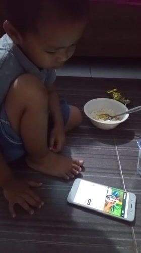 Child sits with smartphone on floor in Lhokseumawe