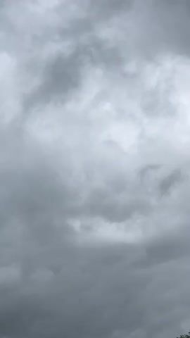 A gray, cloudy sky fills the frame. The clouds are dense and varied in shade, with some appearing lighter and more diffuse, while others are darker and more ominous. There are no discernible objects, people, or actions visible in the video. The environment appears to be outdoors, under an overcast sky. The camera is stationary, focused on the sky.