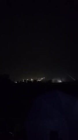 The video is dark and shaky, showing a nighttime scene with faint lights in the distance that appear to be fireworks. In the foreground, a dark blue tarp or umbrella is partially visible. The video is very short and contains minimal detail.