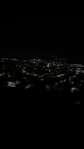 The video begins with a high-angle, static shot of a city at night, with scattered lights indicating buildings and streets. The camera then quickly pans left, blurring the lights into streaks, before abruptly cutting to black.