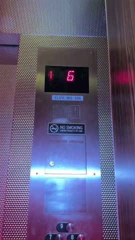Here is a detailed description of the video:

The video shows the inside of an elevator as it travels upwards. The elevator's floor indicator panel displays the current floor number in red digital numerals. The numbers change from 6, to 7, and then to 8. The panel also shows the elevator's number as "ELEV. NO. 166". Below the floor indicator is a "No Smoking" sign and a panel labeled "Firefighters' Operation". The elevator's interior is decorated with a textured metallic material and dark wood paneling. Faint music plays in the background. At the bottom of the panel are floor selection buttons, with the "9" button visible. The camera appears to be stationary, filming the panel directly.