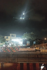 Nighttime aircraft observed flying over lit street with pedestrians