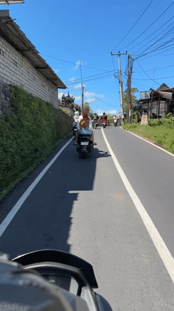 Moped rider travels narrow road in Tampaksiring, Indonesia