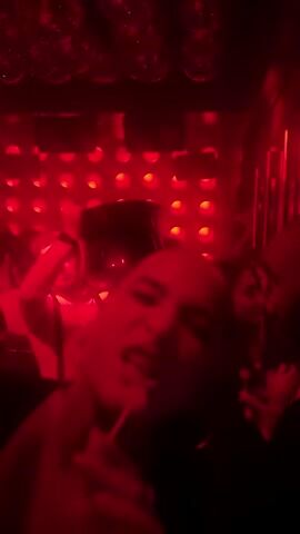 The video shows a crowded, dimly lit club with red and blue strobe lights and disco balls on the ceiling. People are dancing in the dark, with one man in a white shirt and suspenders briefly visible. The lighting alternates between red and blue, making it difficult to discern details. The overall atmosphere is energetic and typical of a nightlife setting.