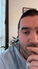 Man bathes pet parakeet in kitchen sink while cat watches