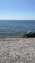 Solitary beachgoer sits by tent on rocky Anapa shore