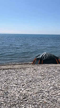 Solitary beachgoer sits by tent on rocky Anapa shore