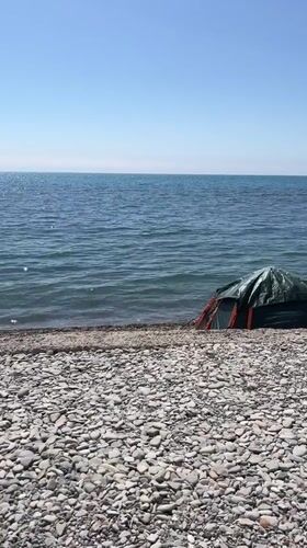Solitary beachgoer sits by tent on rocky Anapa shore