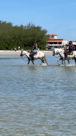 Horseback riders splash through clear waters in Cabo Frio