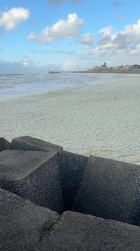 Heavy sea foam blankets The Hague coastline during evening hours