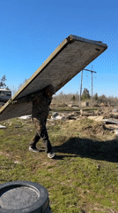 Man carries wooden plank across field in rural Russia