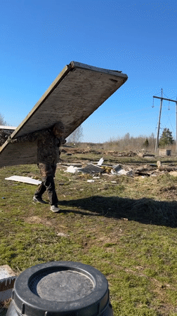 Man carries wooden plank across field in rural Russia