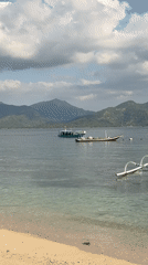 Dive boats anchored off a rocky Indonesian beach at dawn