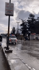 Burnt vehicle blocks wet street in Quetta during rainy day