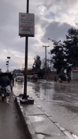 Burnt vehicle blocks wet street in Quetta during rainy day