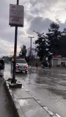 Burnt vehicle blocks wet street in Quetta during rainy day