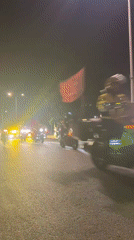 Nighttime motorcycle procession with Vietnamese flags observed on city streets