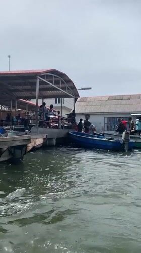 Blue boat departs Ibasa waterfront past industrial shoreline
