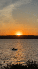 Sunset over water witnessed by couple with stroller, boats visible