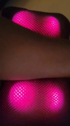 A person's arm is resting on a massage pillow or cushion. The device is illuminated with two pink lights shining through a mesh fabric cover.