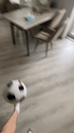Baby and adult pass a toy soccer ball on a home floor