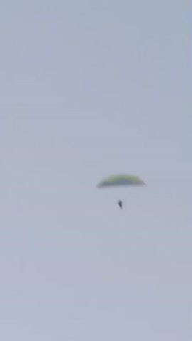 This video captures a paraglider soaring against a hazy, overcast sky. The paraglider, a small, dark silhouette, is suspended beneath a colorful wing, predominantly yellow and green, which is slightly blurred due to the movement and possibly atmospheric conditions. The scene is entirely focused on the paraglider and the expansive sky, with no discernible ground features or other objects visible.

The activity is clearly paragliding, a recreational activity involving a parachute-like wing and a harness for the pilot to sit in. The flight appears to be a gentle descent or cruise, with the paraglider maintaining a relatively stable position against the backdrop of the sky.

The time of day is not explicitly indicated, but the diffused light suggests it could be daytime, possibly morning or late afternoon, or a particularly cloudy period. The weather appears to be overcast, contributing to the uniformly light gray sky and the slight haziness. The location is given as Wilkasy, Poland, but there are no visual cues within the video to confirm this specific geographical context. The overall mood is one of serene isolation, with the paraglider appearing small and alone in the vastness of the sky. There is no visible text in the media file.