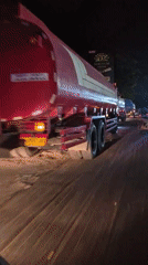 Two tanker trucks drive slowly through Lhokseumawe streets at night