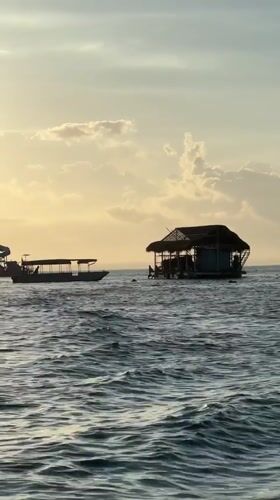 Boat passengers wave near traditional sea platform off Nusa Penida