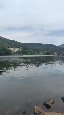 A slow pan of a lake with mountains in the background. A building can be seen on the side of the mountain. The sky is overcast.