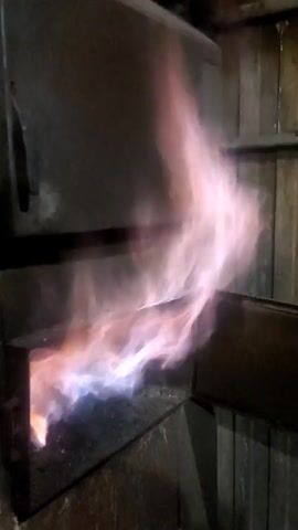 The video shows an industrial furnace with a large, swirling flame. The flames are colored in shades of pink, white, and blue, and they appear to be burning intensely. The furnace itself is made of dark metal. The environment appears dark and enclosed.