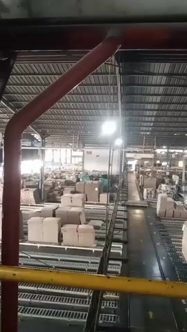 The video shows a panoramic view of a large warehouse filled with stacks of boxes and pallets. The warehouse has a high ceiling with industrial lighting. Conveyor belts are visible, suggesting an automated system for moving goods. In the distance, some machinery can be seen. A sign that reads "HYDRANT" is hanging from the ceiling. The overall impression is one of a busy, operational storage or distribution facility.