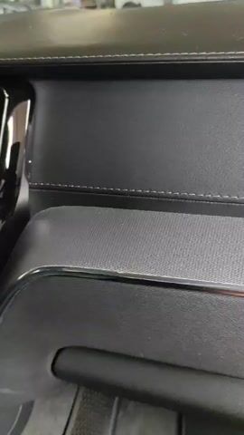 A close-up video shows a car's interior dashboard. The camera pans across the central console, focusing on the air vents, a large infotainment screen, and the gear shifter. The dashboard is primarily black with stitched leather accents. The video also captures glimpses of the steering wheel and surrounding components, suggesting a modern vehicle interior.