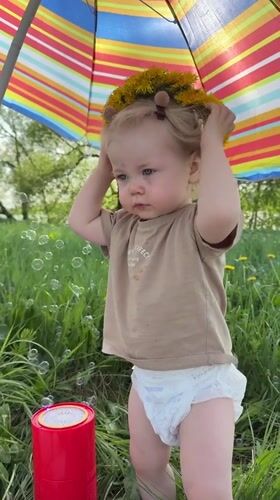 Toddler plays under umbrella in Vladimir field