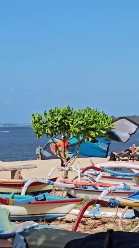 Kiteboarders and fishing boats on a Denpasar beach morning